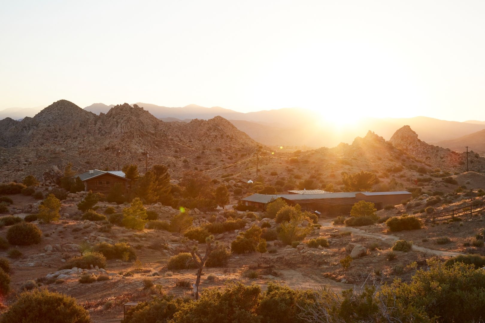 The ESCAPE compound at golden hour — wood buildings tucked into the high desert ridge, mountains beyond