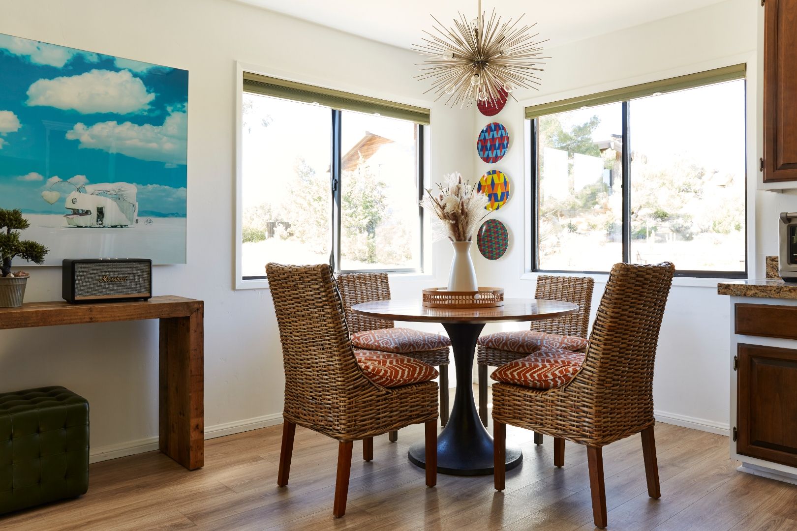 The Cottage dining nook at ESCAPE — rattan chairs around a tulip table, Salt Flats artwork, sputnik chandelier, desert through the windows