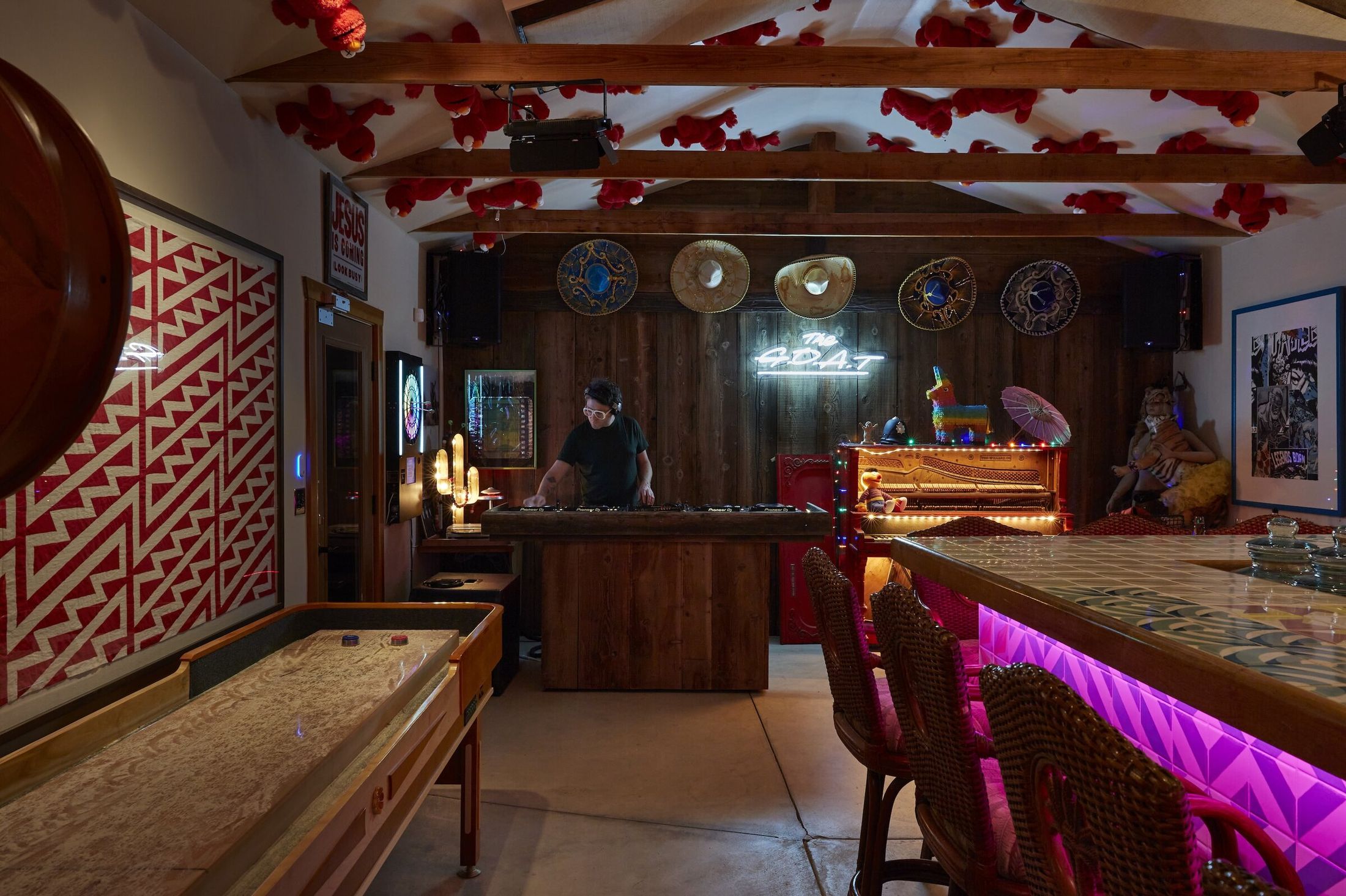 The GOAT bar at ESCAPE — DJ behind the decks, neon GOAT sign, lit-up red piano, pink bar glow, sombreros on the wall, shuffleboard