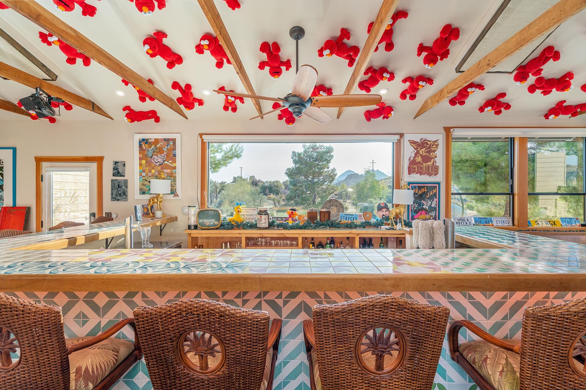 The GOAT bar at ESCAPE looking out the picture window to the desert — tiled bar top, wicker stools, ceiling Elmos overhead