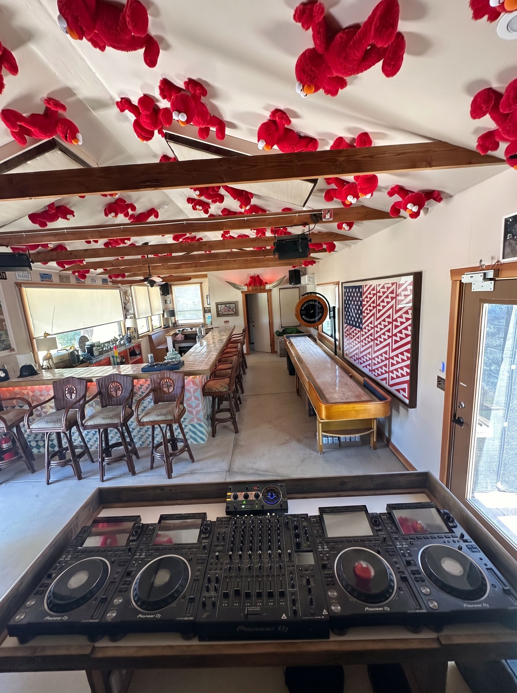 The four-deck Pioneer DJ rig at The Goat at ESCAPE — view from behind the decks across the tiled bar, wicker stools, shuffleboard and Elmo-covered ceiling